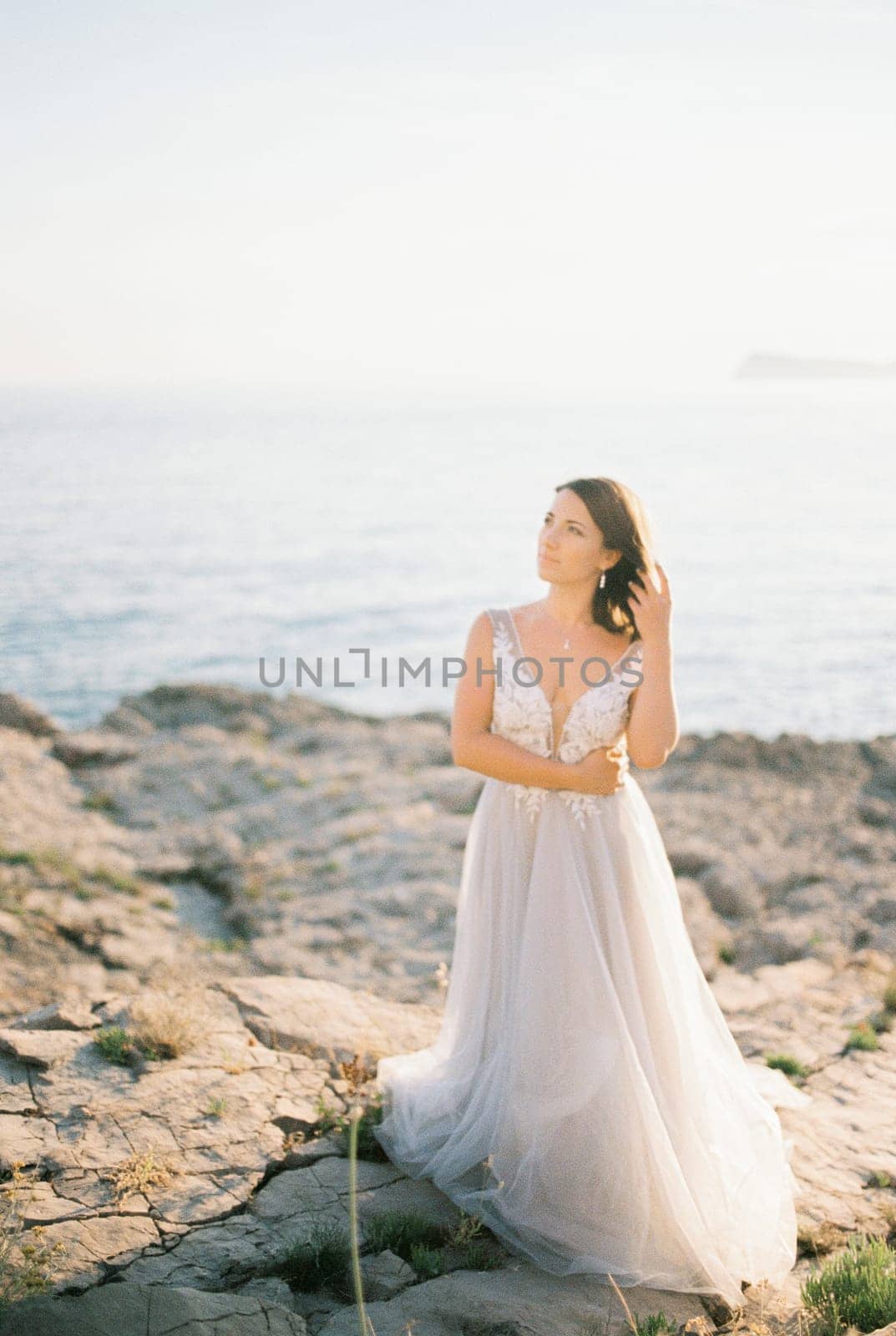 Bride in a white puffy dress stands on a rocky seashore. High quality photo