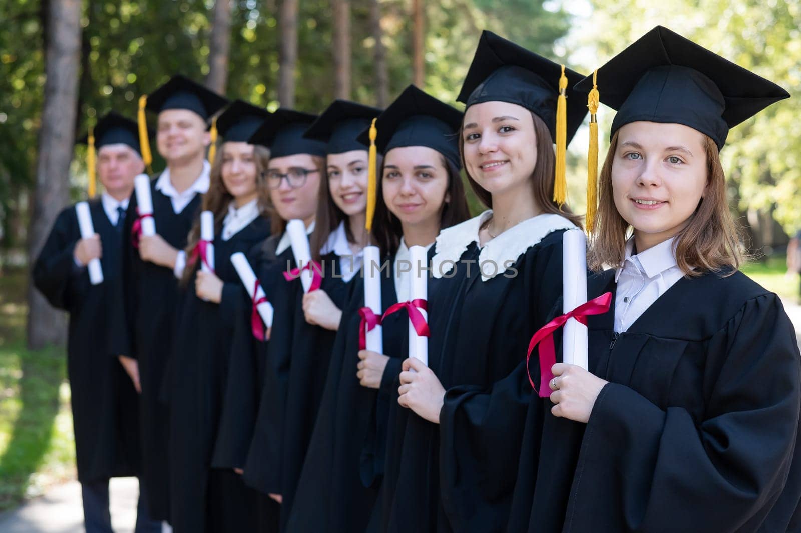 Row of young people in graduation gowns outdoors. Age student