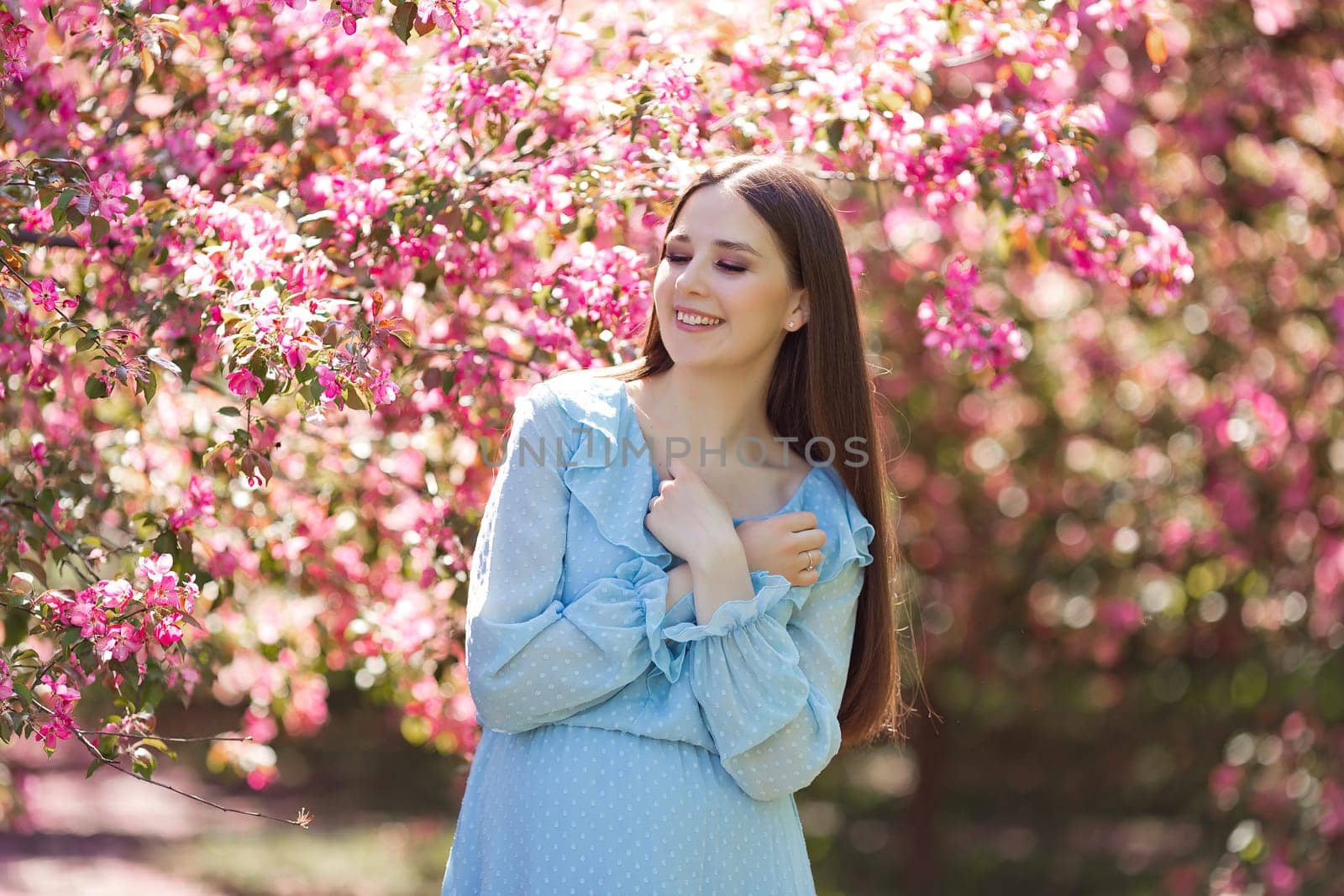 A happy smiling girl, long hair, standing in a pink blooming garden by Zakharova