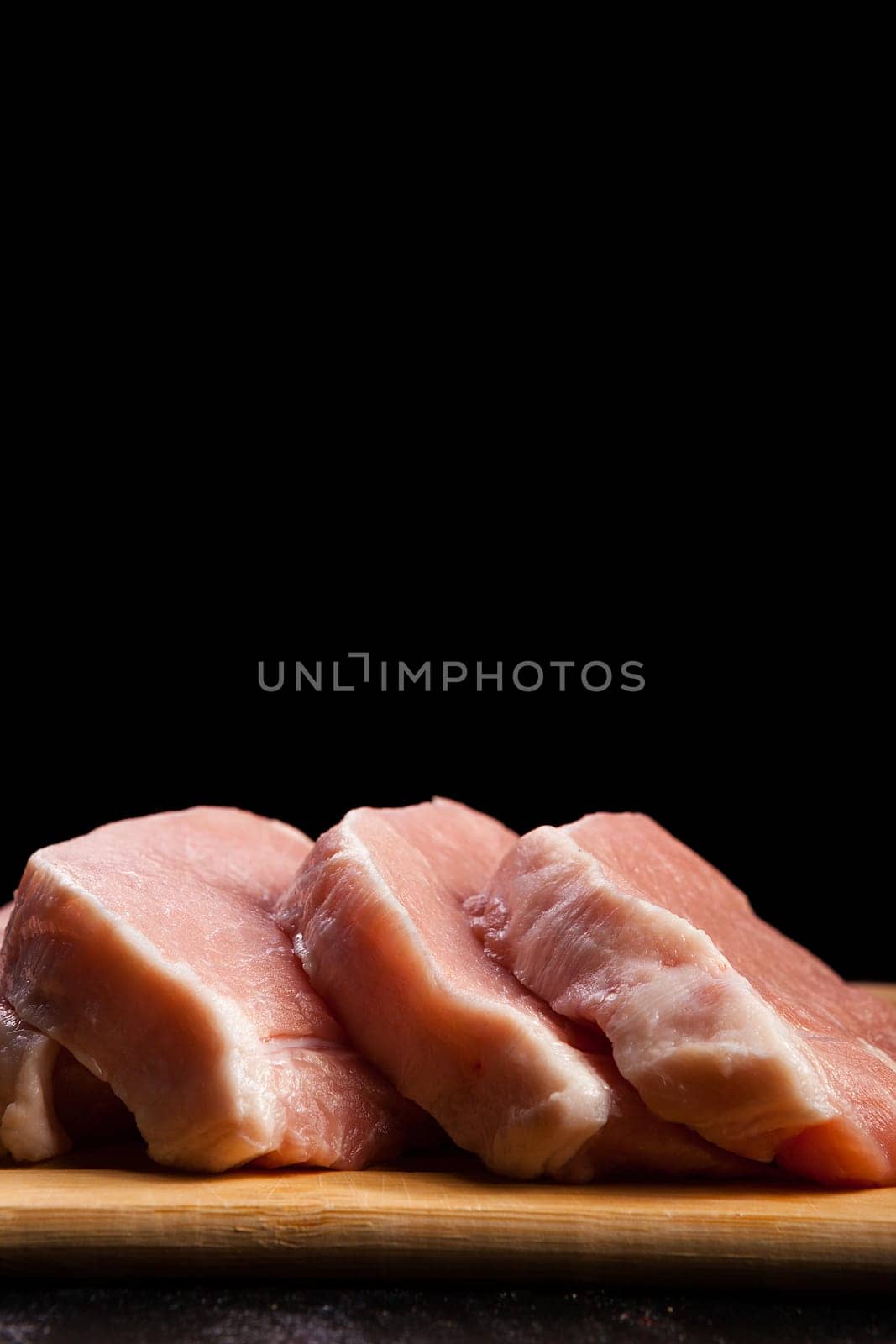four pieces of fresh raw meat on wooden board on black wooden background. Gourmet food and fresh uncooked meal