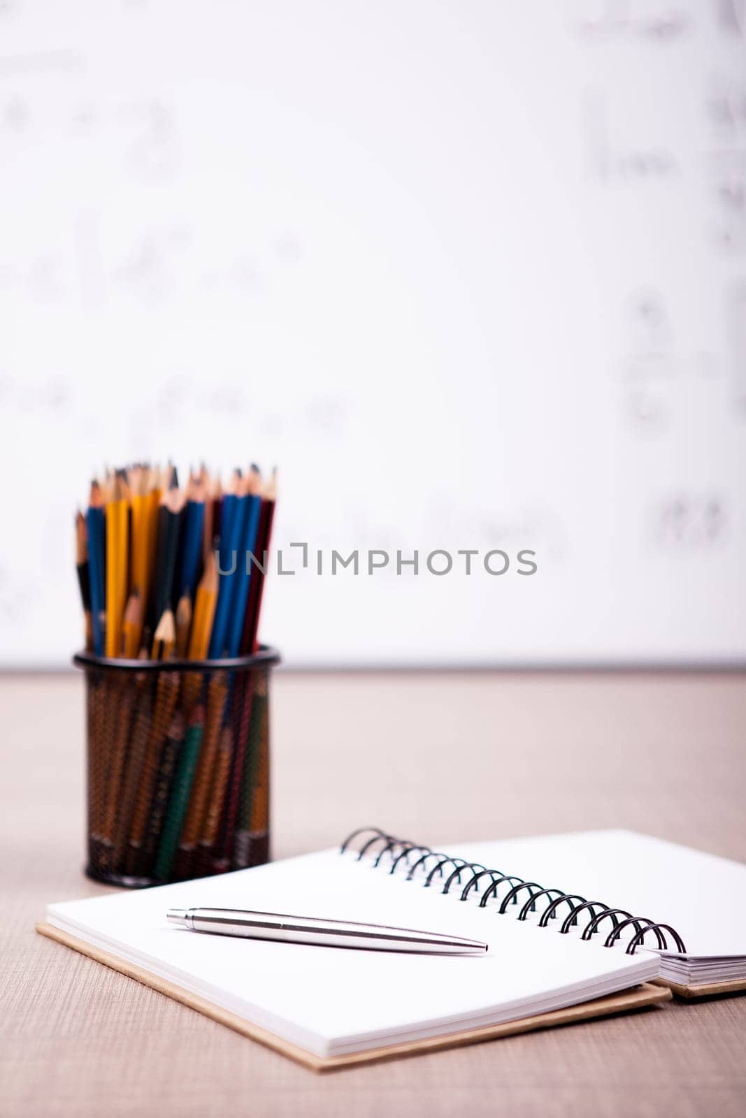 Books, notebook and pencils on table with a blurred white board in the back. School concept