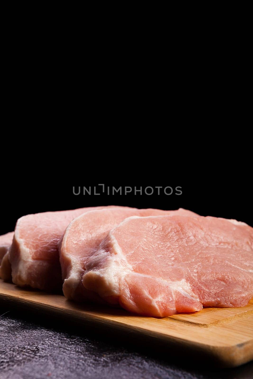 four pieces of fresh raw meat on wooden board on black wooden background. Gourmet food and fresh uncooked meal