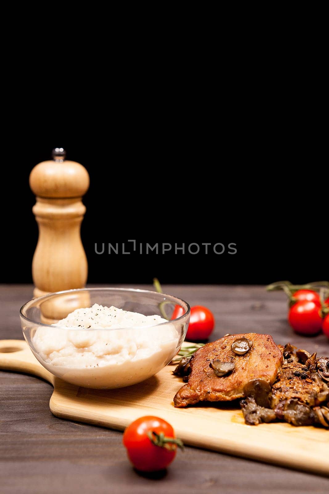 Grilled pork steak, mushrooms cherry tomatoes and a plate with bean paste on wooden plate on a table in studio photo on black background