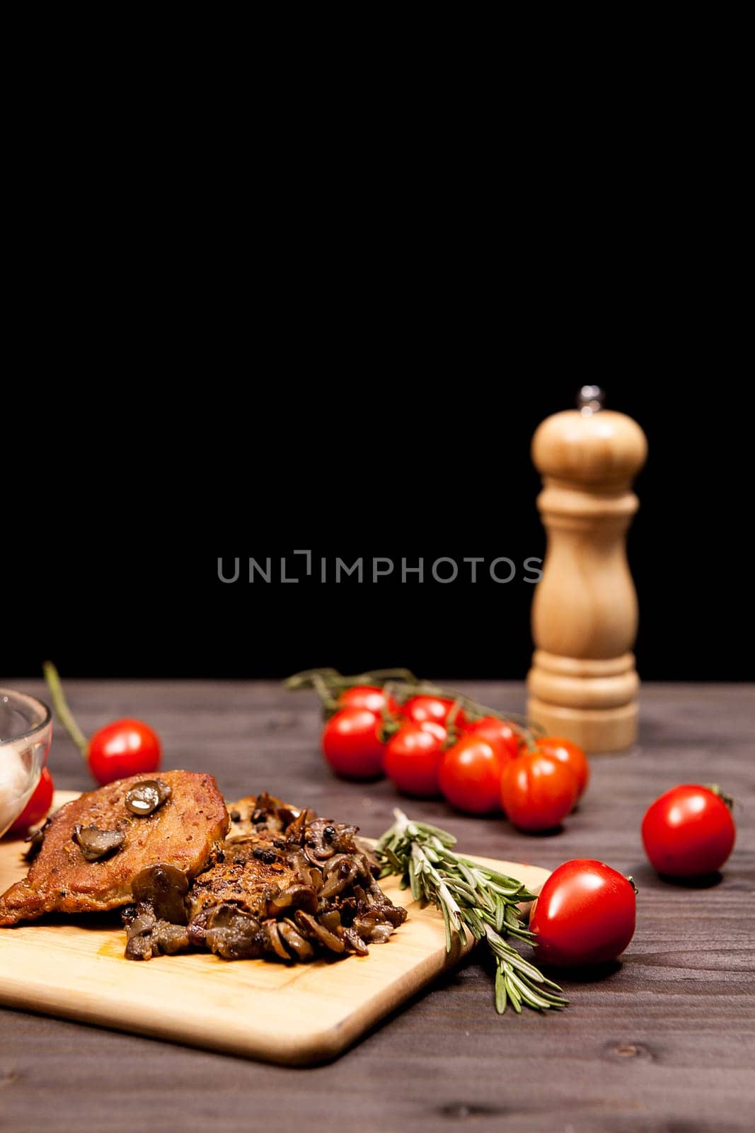 Grilled pork steak, mushrooms cherry tomatoes and a plate with bean paste on wooden plate on a table in studio photo on black background