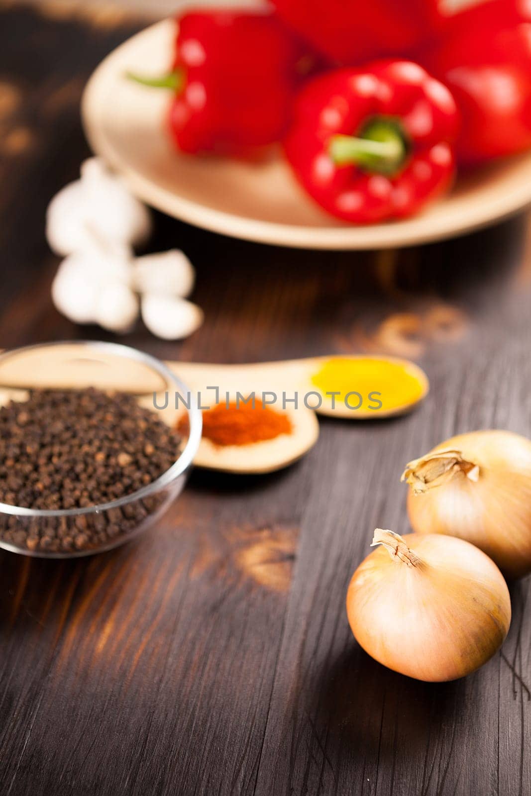 Top close up view on onions with different vegetables blurred on background over burned wooden table