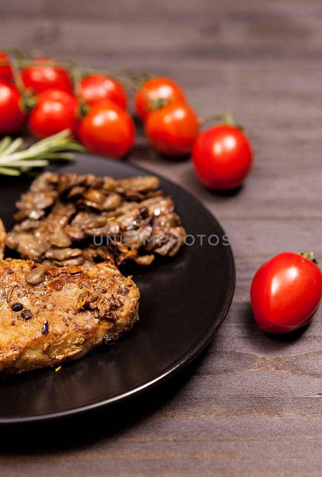 Roasted Pork steak in black plate with grilled mushrooms, oregano cherry tomatoes and bean paste on a wooden table