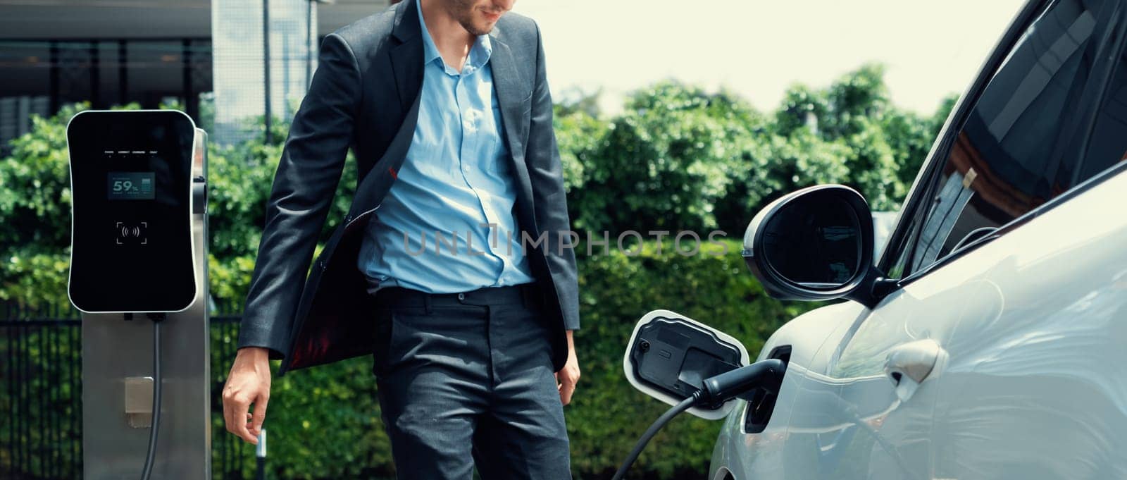 Progressive businessman with EV car at public parking car charging station. by biancoblue