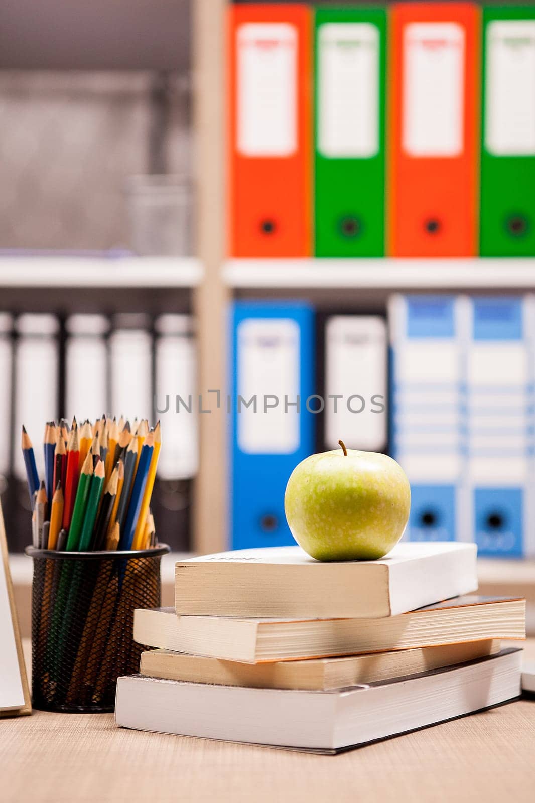 Green apple on pile of books next to a notebook and pencils on t by DCStudio
