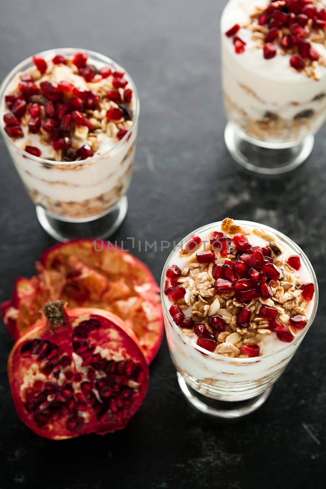 Three glasses filled with home made muesli on top with pomegranate on dark wooden background