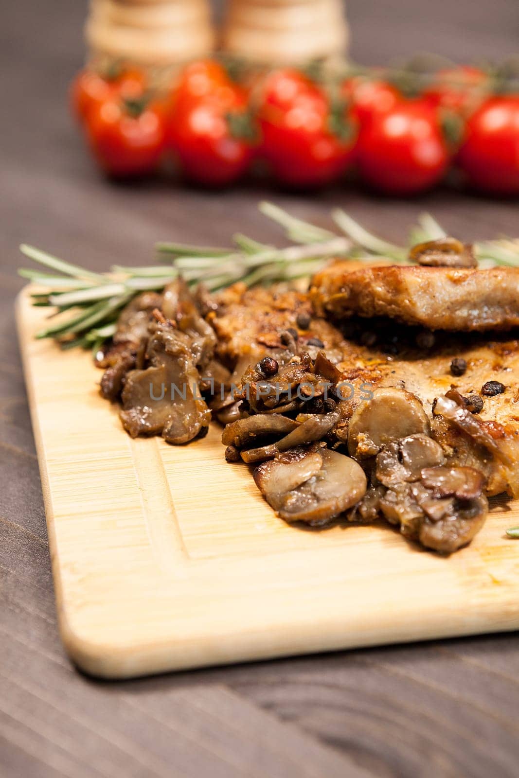 Close up image on pork steak on wooden board next to grilled mushrooms and cherry tomatoes