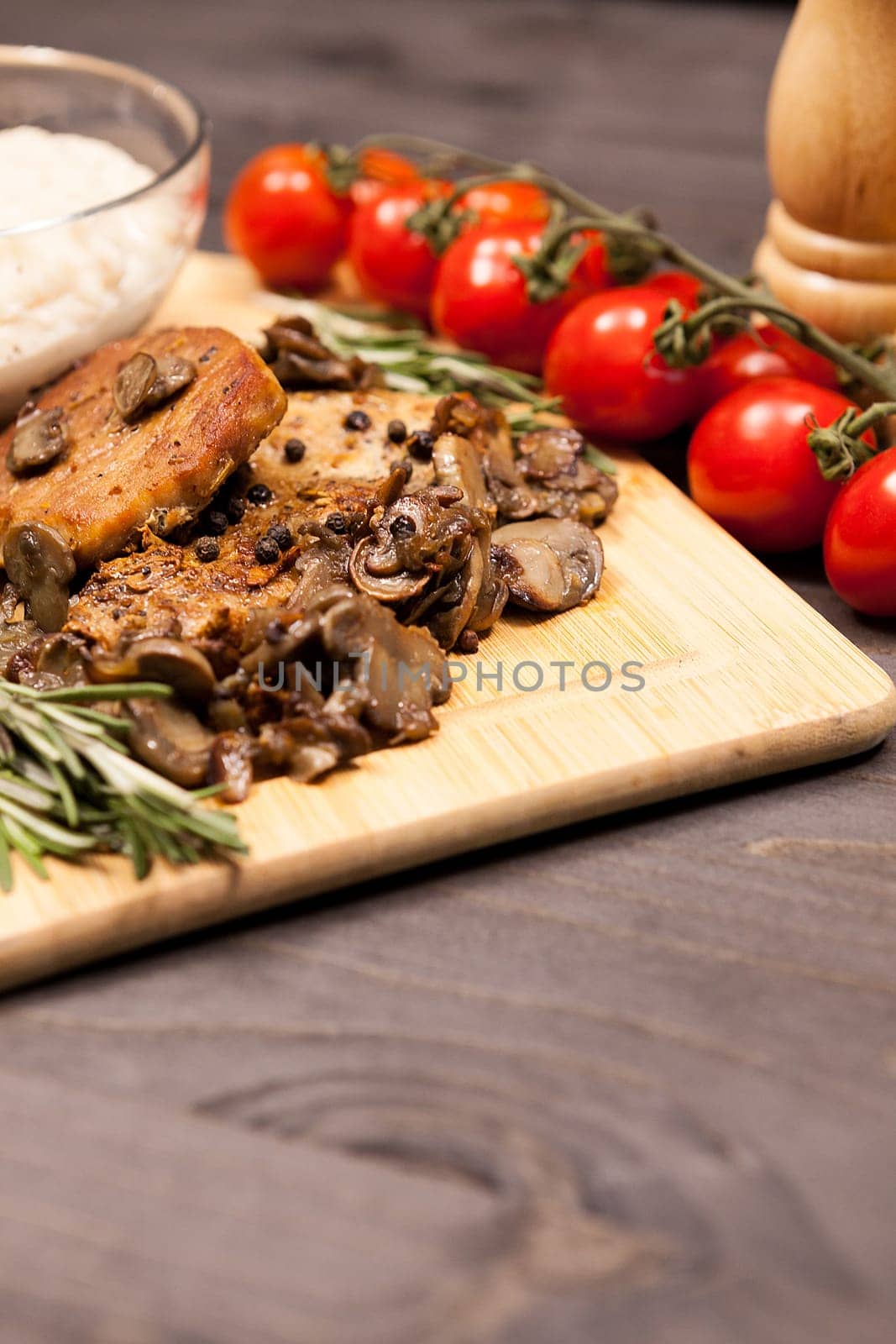 Grilled pork steak, mushrooms and cherry tomatoes and a plate with bean paste on wooden plate on a table