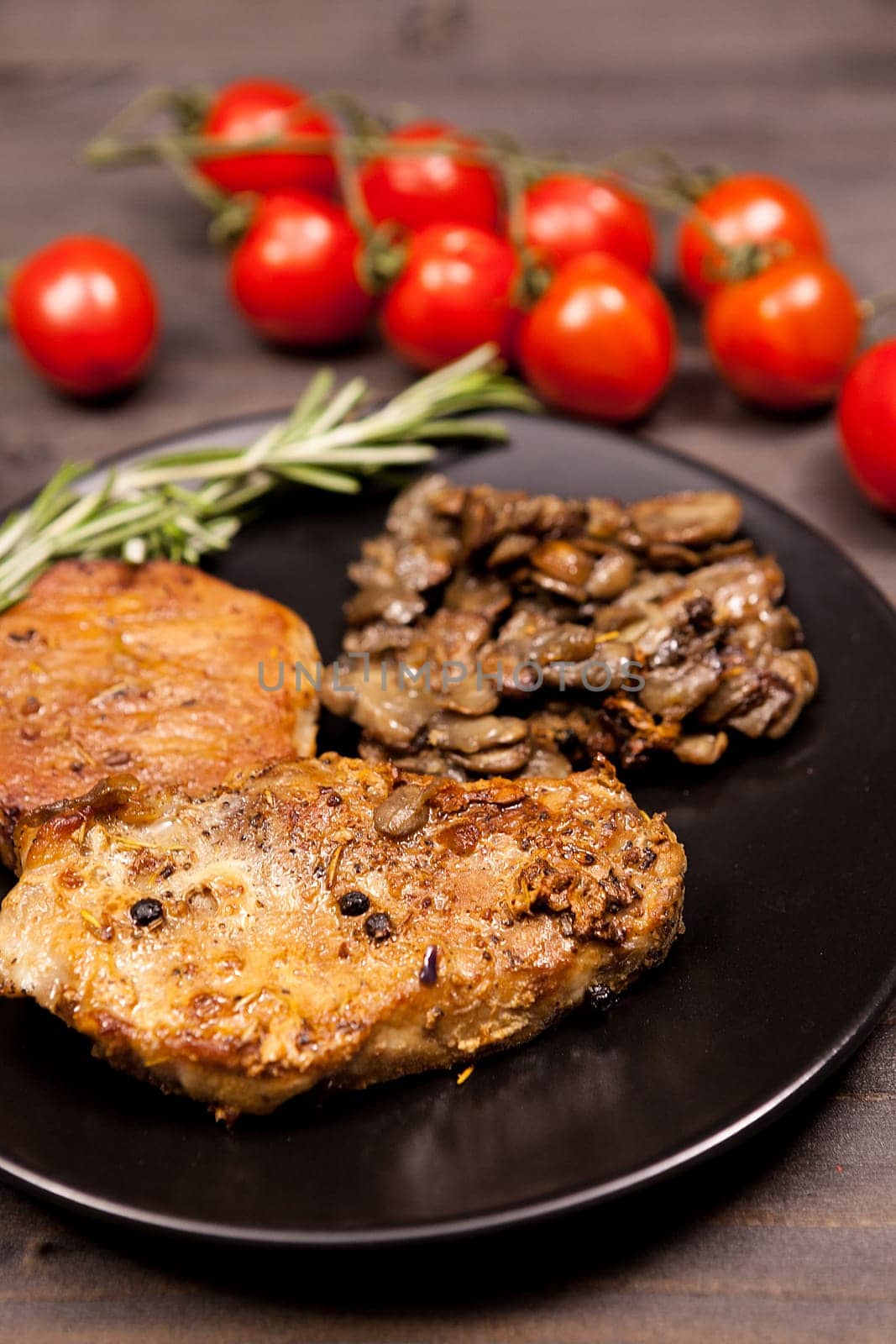 Roasted pork in black plate with grilled mushrooms, oregano cherry tomatoes and bean paste on a wooden table