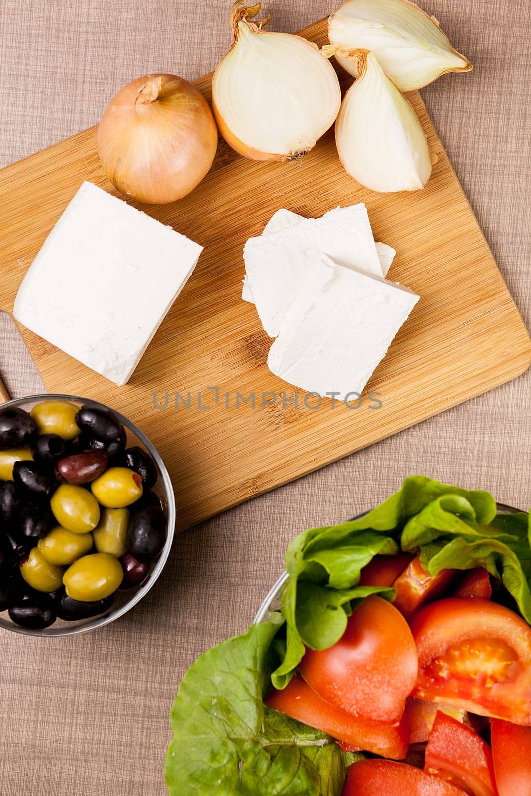 Top view of feta white cheese on wooden board on a table whith olives, summer salad and cut onions