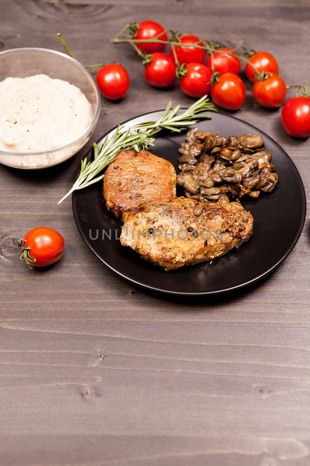 Pork steak in black plate with grilled mushrooms, oregano cherry by DCStudio