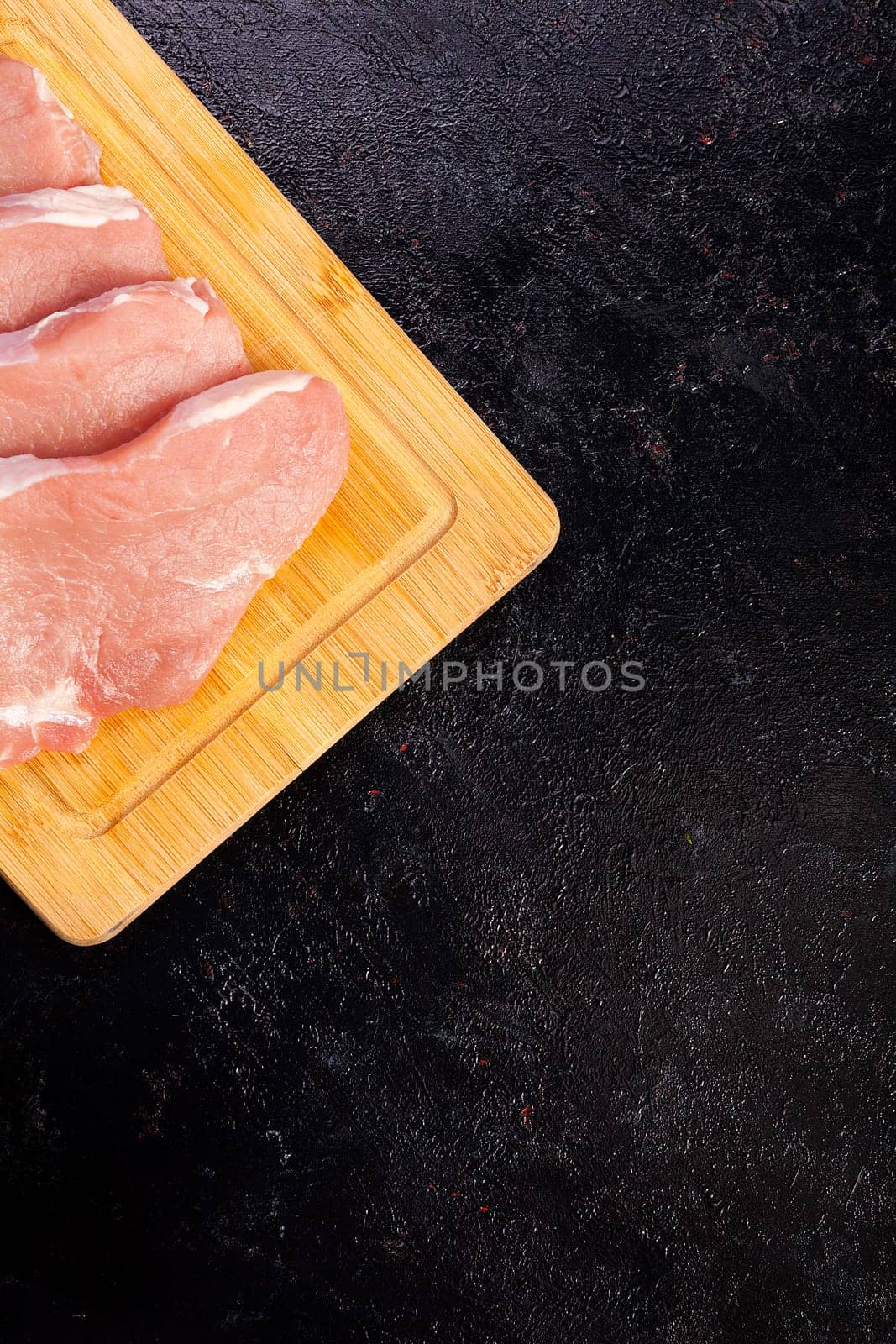 Over top view of fresh raw meat on wooden board on black wooden background. Gourmet food and fresh uncooked meal
