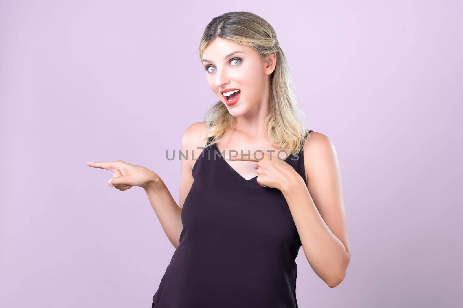 Alluring portrait of beautiful woman with perfect makeup clean skin point finger side way in pink copyspace isolated background. Promotion indicated by hand gesture concept for skincare advertisement.