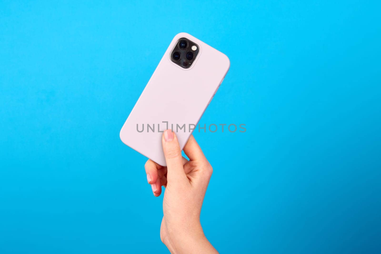 Hand of unrecognizable person showing back side of modern silver smartphone against blue backdrop in studio