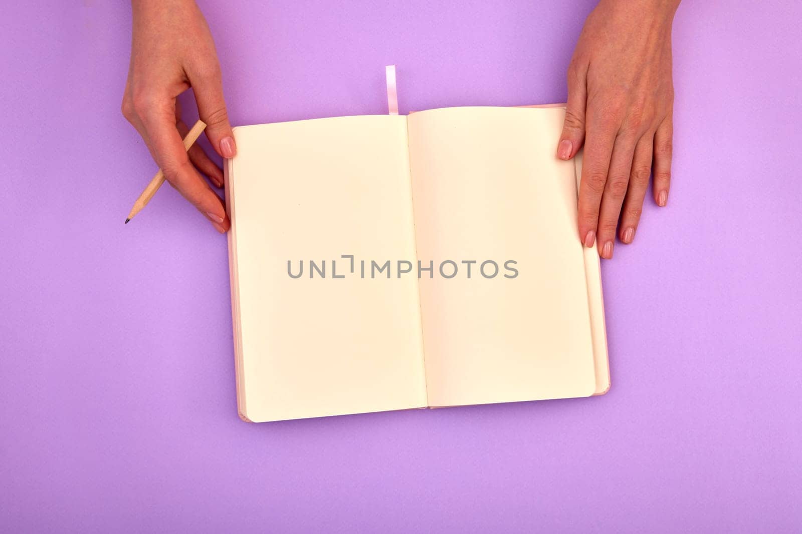 Overhead view of crop person with pencil touching opened notebook against violet background while going to write on blank pages