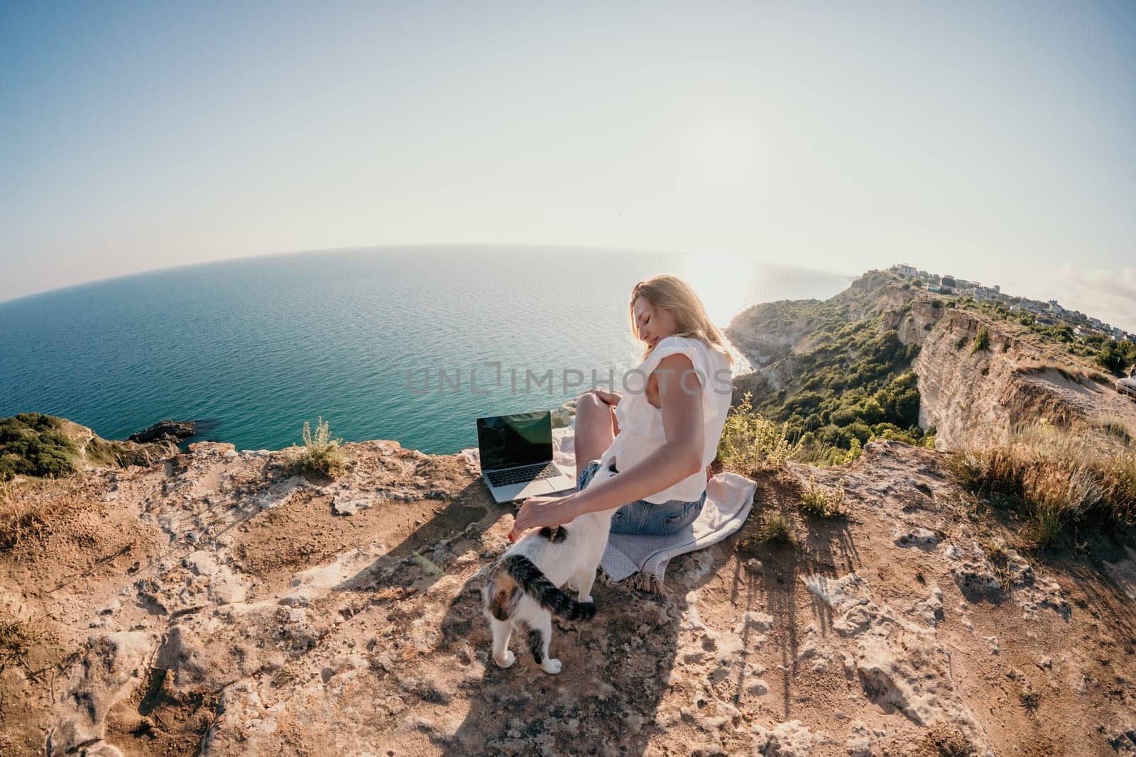 Woman sea laptop. Business woman petting cat and working on laptop by the sea. Close up on hands of pretty lady typing on computer outdoors summer day. Freelance, digital nomad and holidays concept. by panophotograph