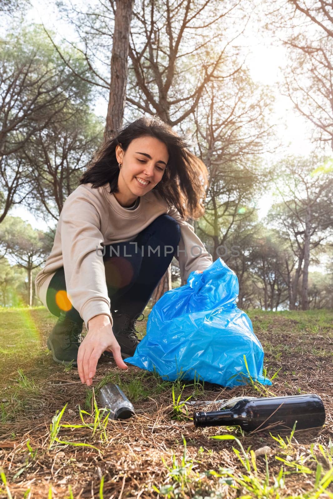 Happy young caucasian woman pick up plastic bottle in the forest. Vertical image.Environmental activist concept.