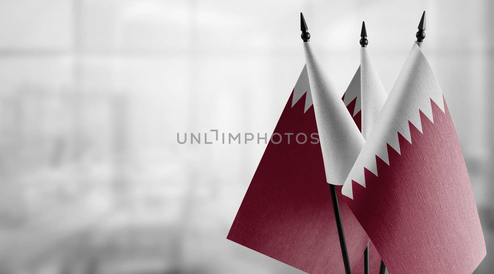Small flags of the Qatar on an abstract blurry background.