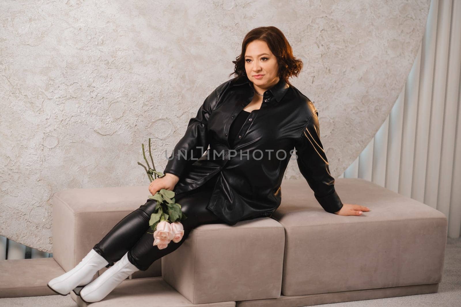 a stylish adult woman in black leather clothes is sitting with a bouquet of pink roses in the interior by Lobachad