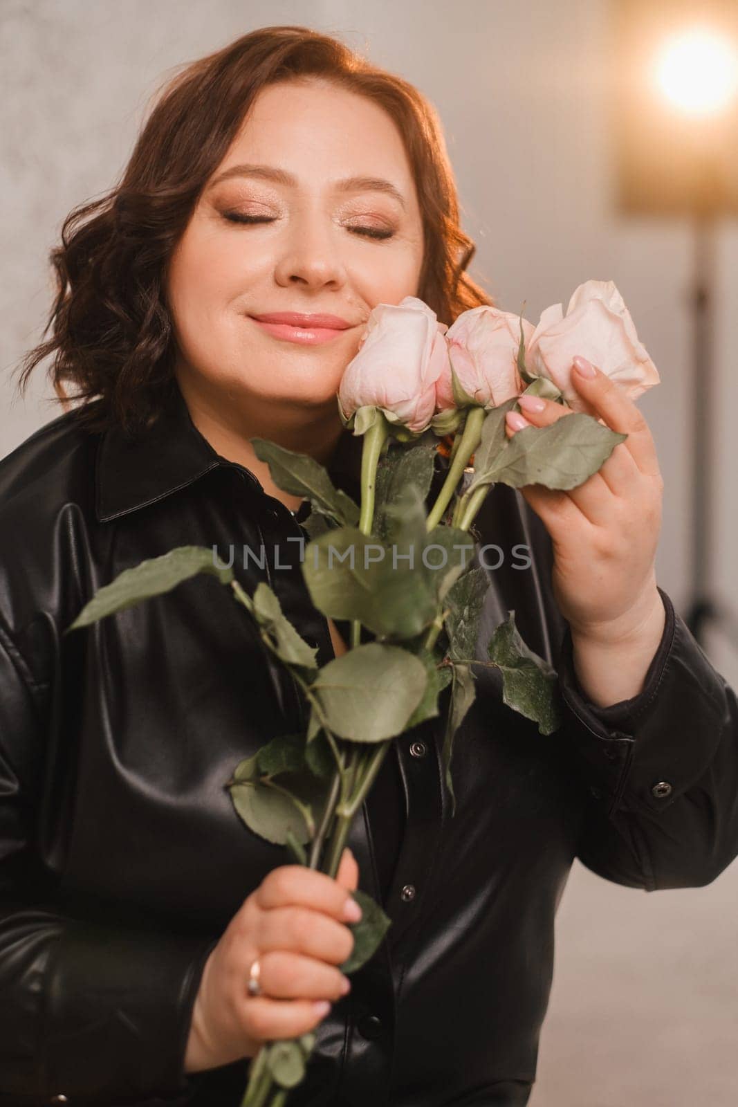 a stylish adult woman in black leather clothes stands with a bouquet of pink roses in the interior.