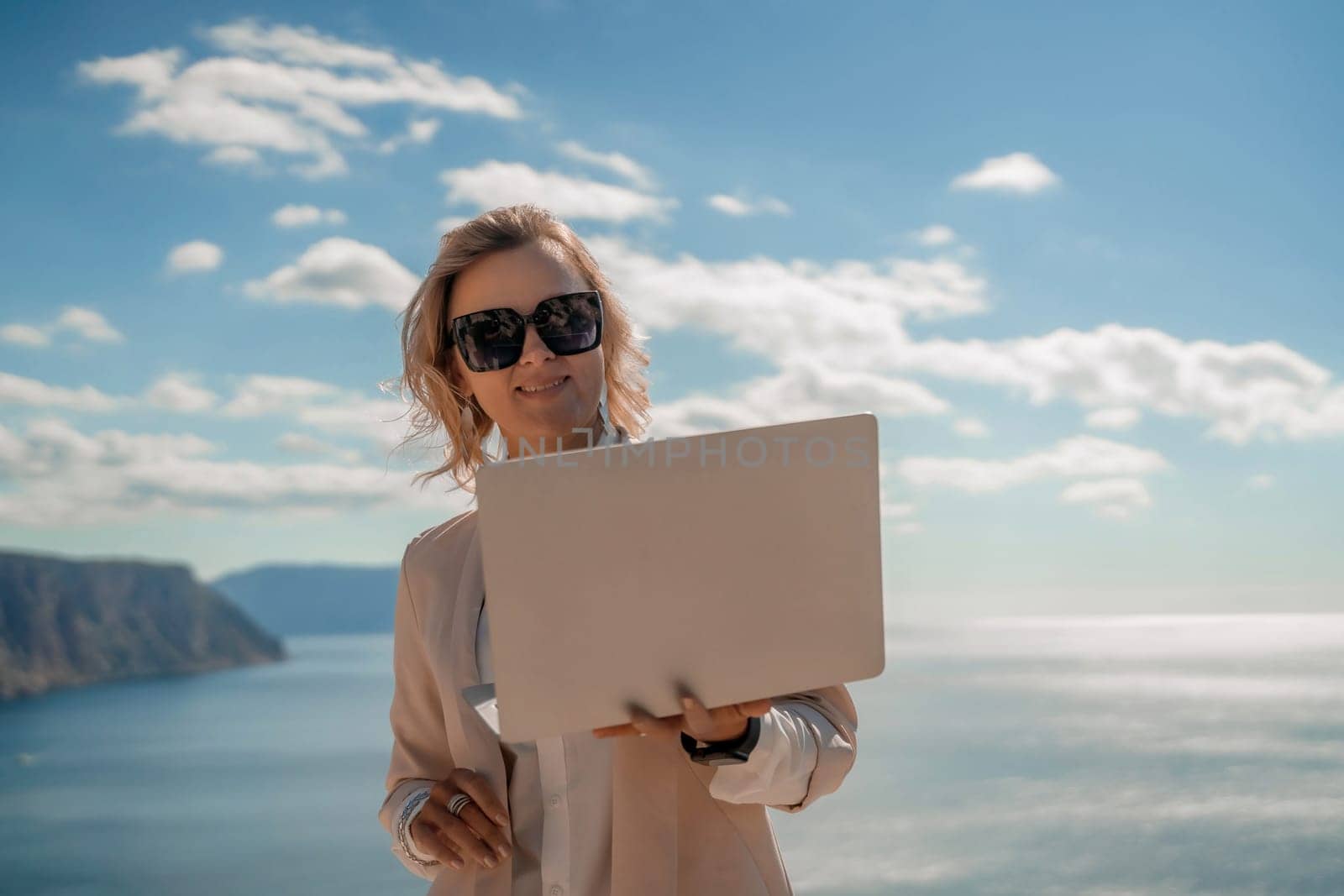 Freelance women sea. She is working on the computer. Good looking middle aged woman typing on a laptop keyboard outdoors with a beautiful sea view. The concept of remote work