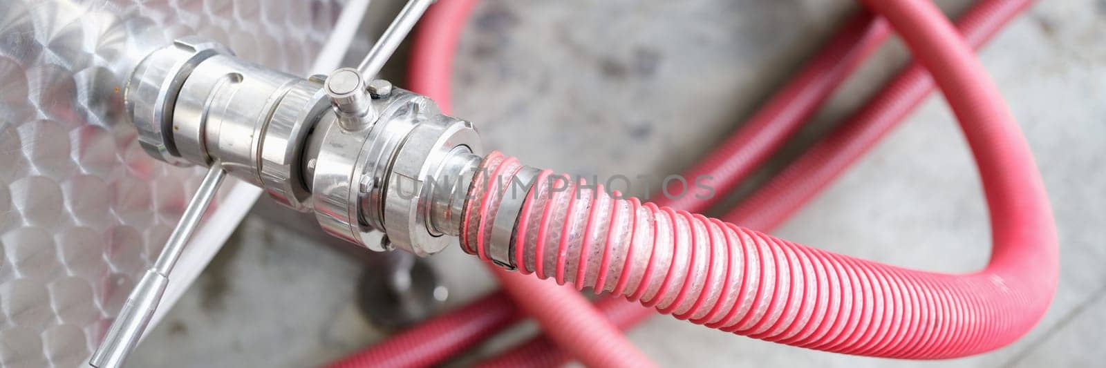 Red faucet connected to steel barrel in factory closeup. Chemical industry concept