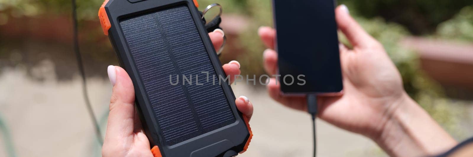 Female hand holding solar power bank and mobile phone closeup by kuprevich