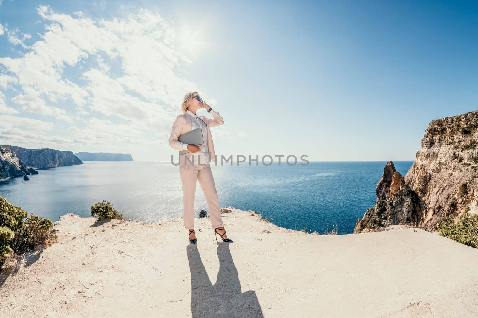 Digital nomad, Business woman working on laptop by the sea. Pretty lady typing on computer by the sea at sunset, makes a business transaction online from a distance. Freelance, remote work on vacation by panophotograph