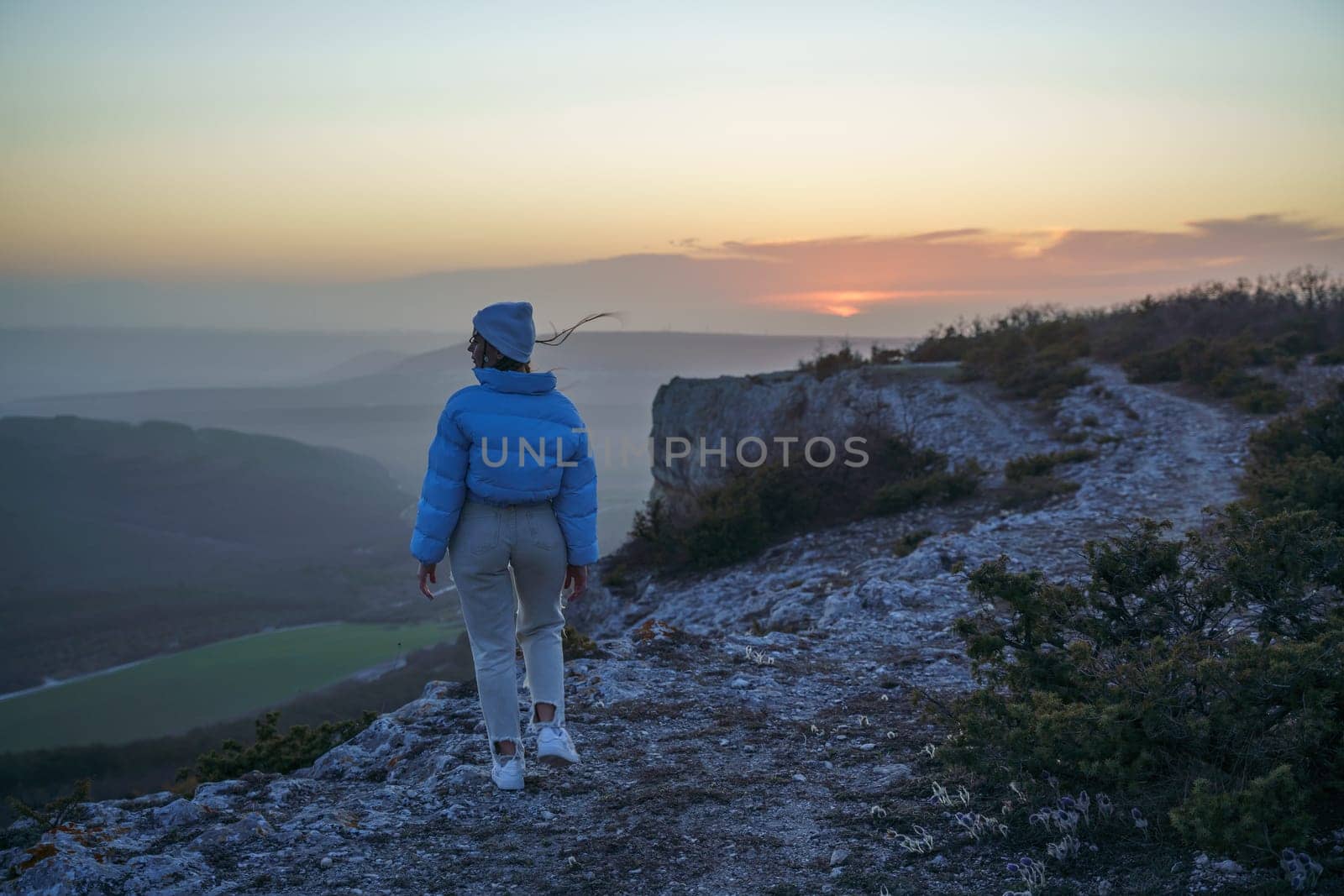 Woman tourist on top of sunrise mountain. The girl salutes the sun, wearing a blue jacket, white hat and white jeans. Conceptual design. by Matiunina