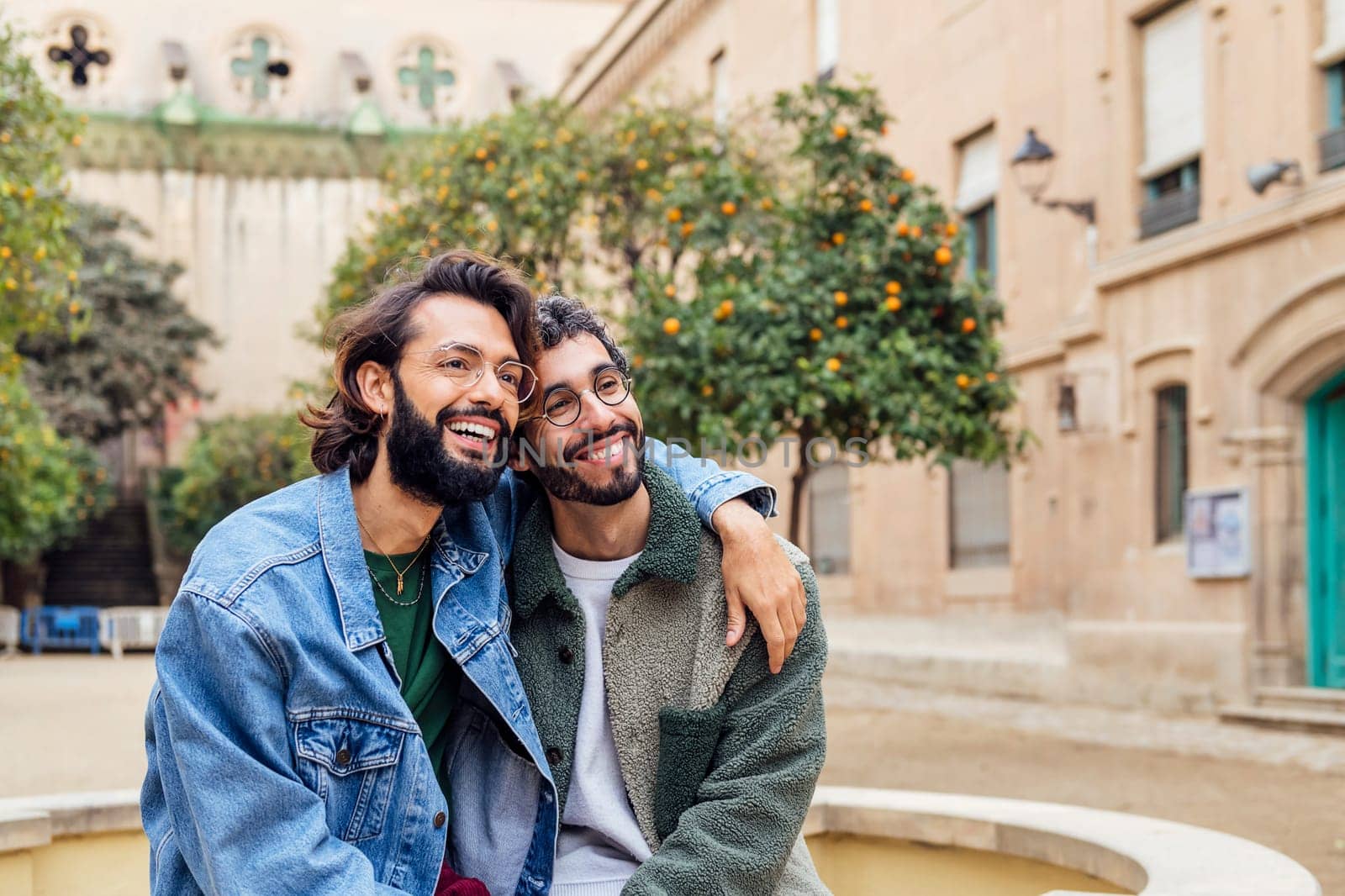 couple of gay men smiling happy sitting in a park hugging, concept of urban lifestyle and love between people of the same sex