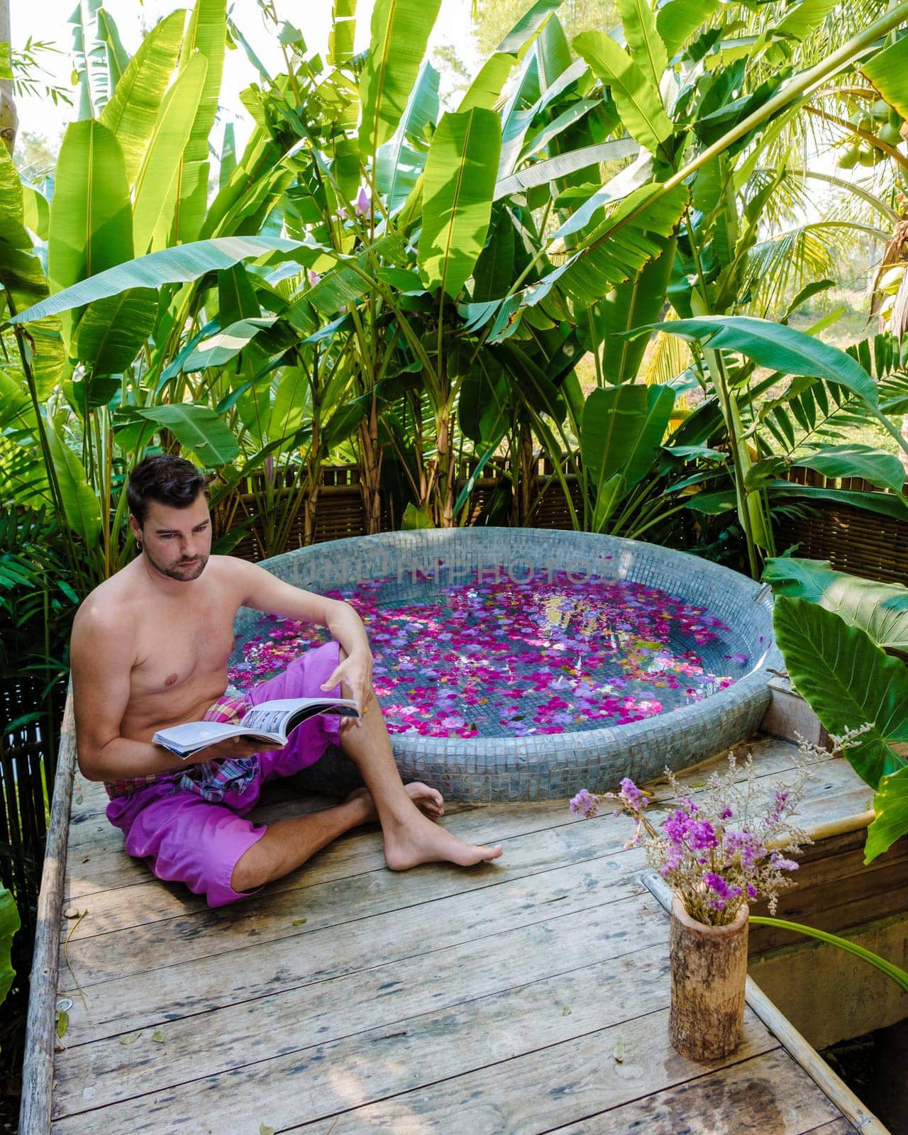 Men reading a book at a bathtub in the rainforest of Thailand during vacation by fokkebok