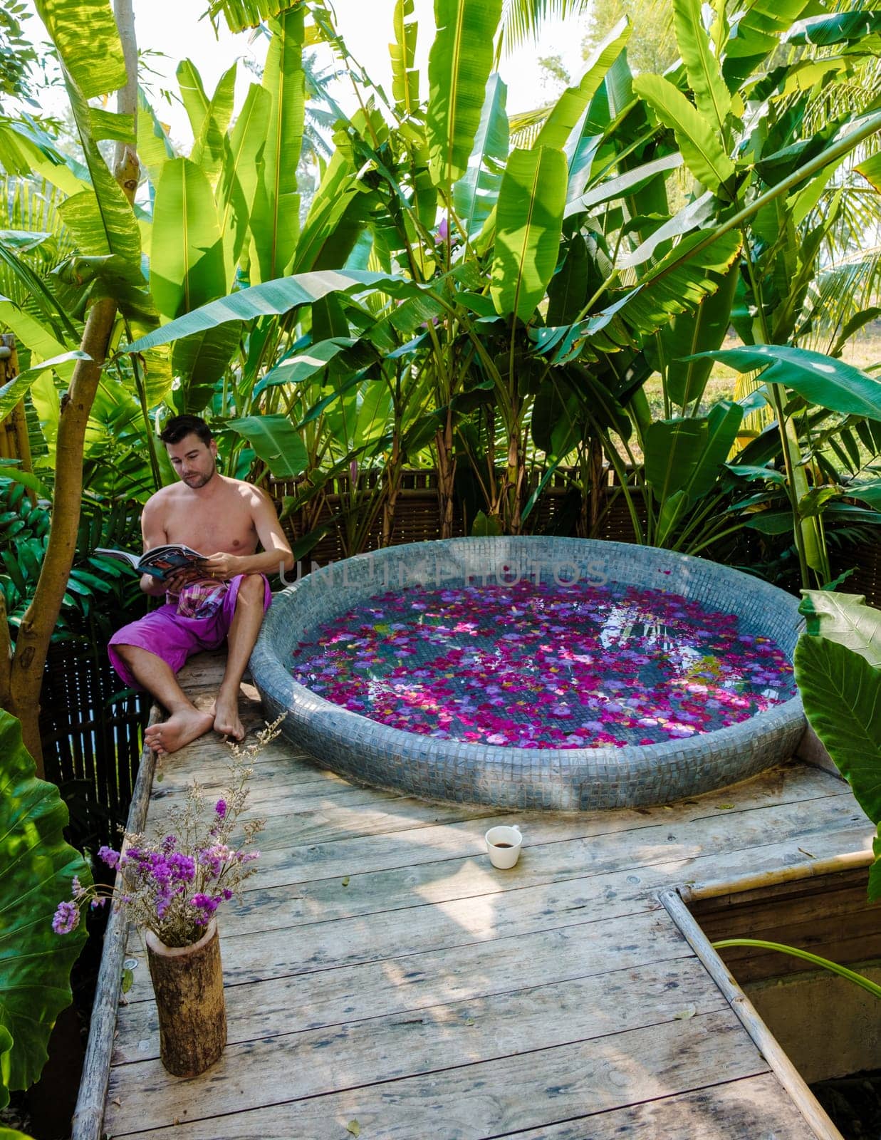 men reading a book at a bathtub in the rainforest of Thailand during a vacation with flowers in the bath