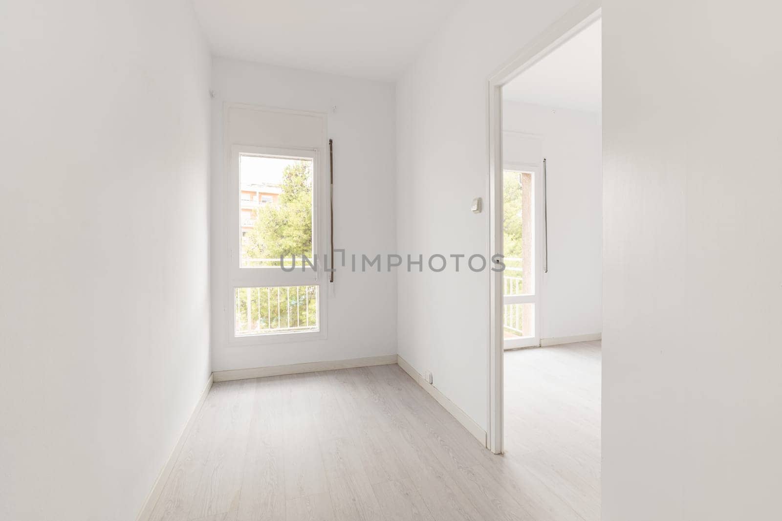 View of an empty white bright room with window without furniture after painting and renovation with wooden floor and baseboards. Concept of beautiful laconic interior for various inspiring ideas.