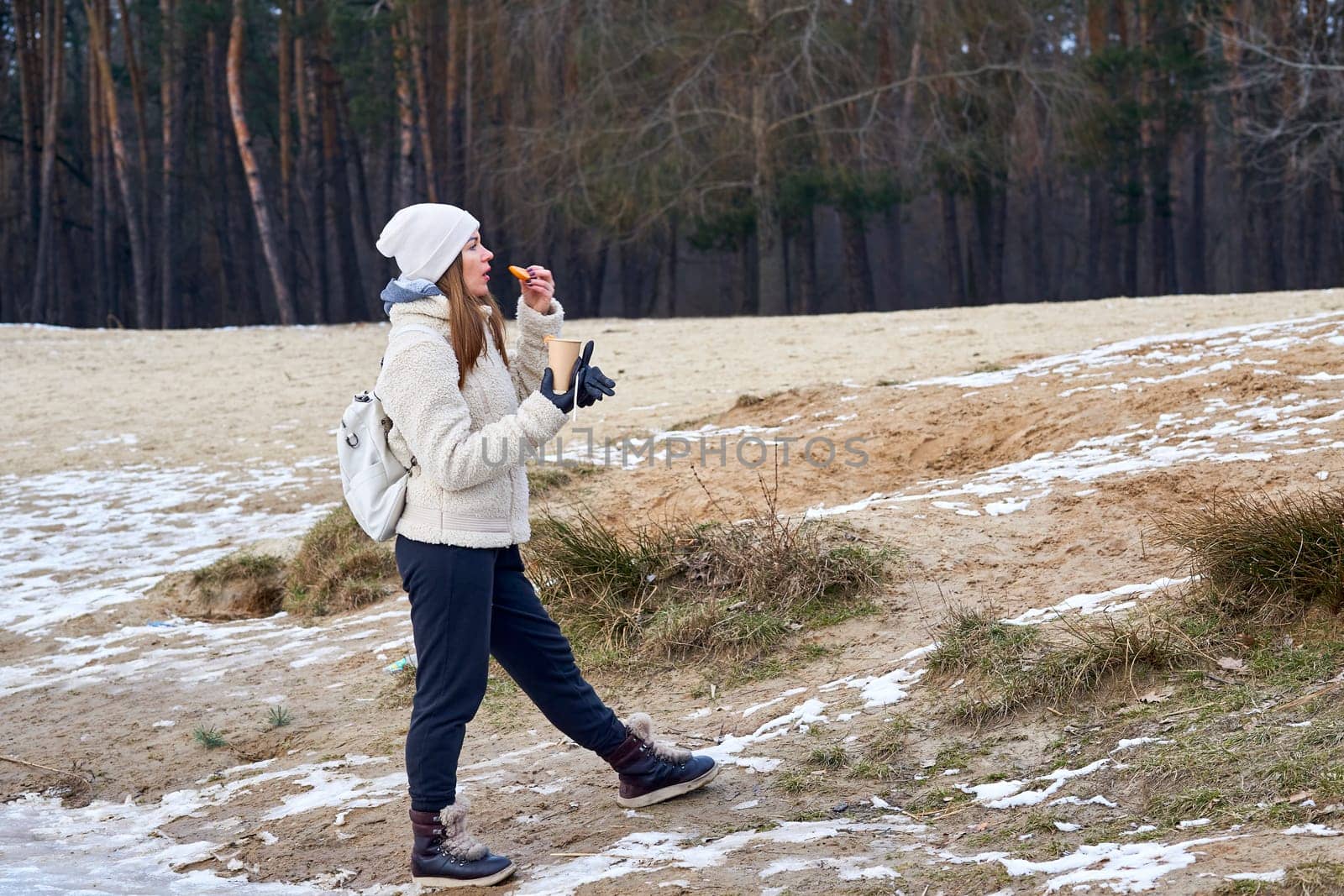 a small amount of food eaten between meals. Young woman hiker having a snack while hiking in spring winter autumn forest.