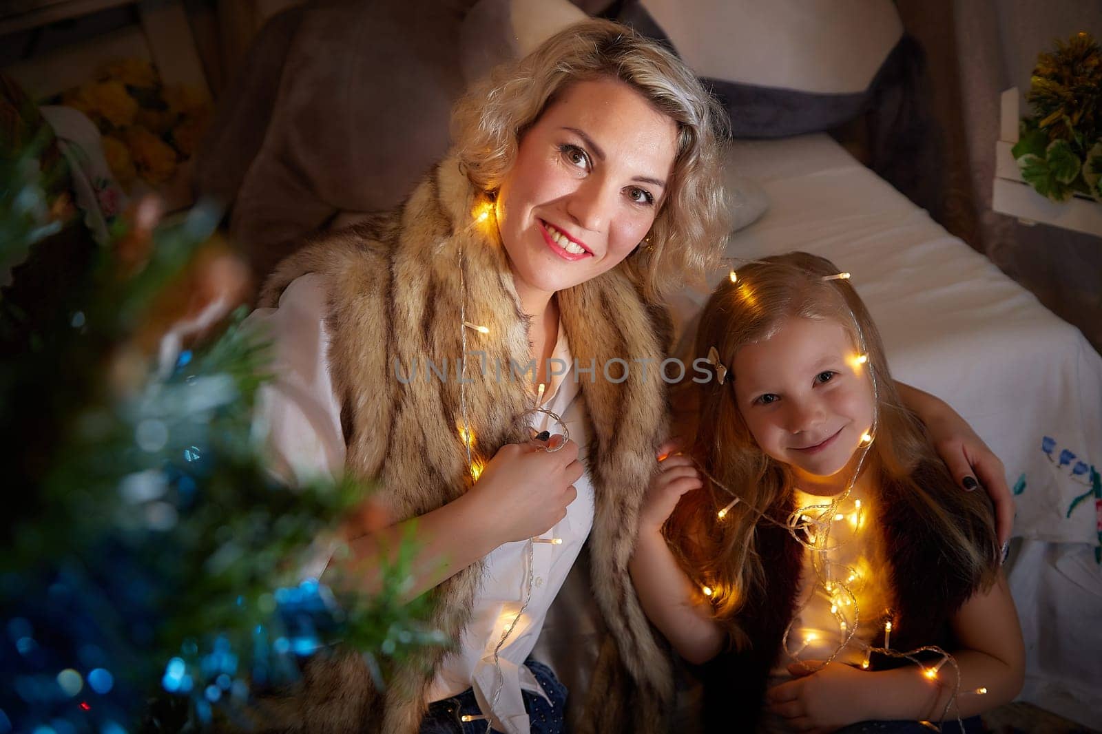 Cute mother and daughter in a room with Christmas garlands. The tradition of decorating the house and dressing up for the holidays. Gifts for family. Happy childhood and motherhood