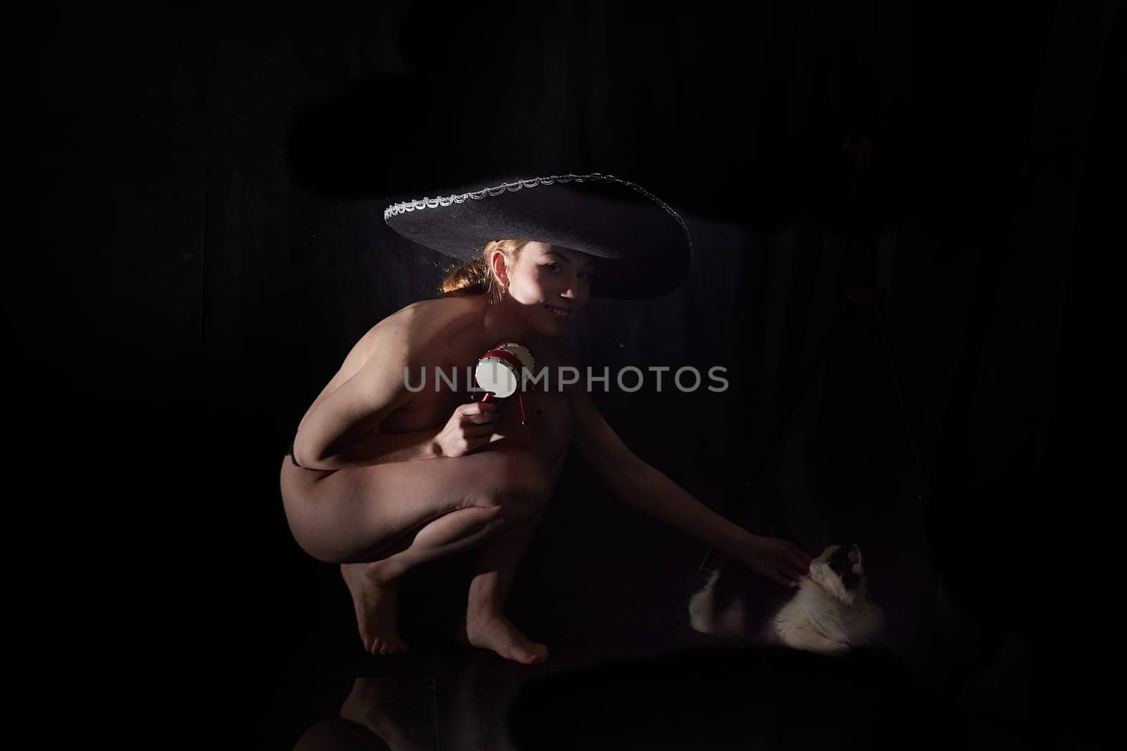 Beautiful slim naked girl in hat and in underwear with a domestic cat on a black background in photo studio by keleny