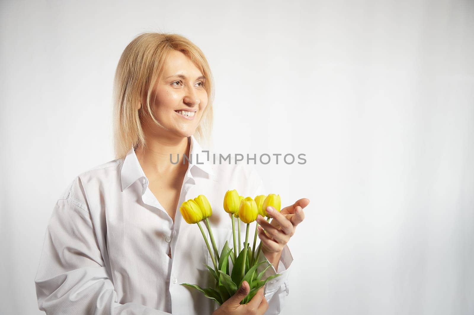 Beauty young blonde happy woman with bouquet of yellow tulips on white background. The concept of a holiday and a gift for a lady and a girl by keleny