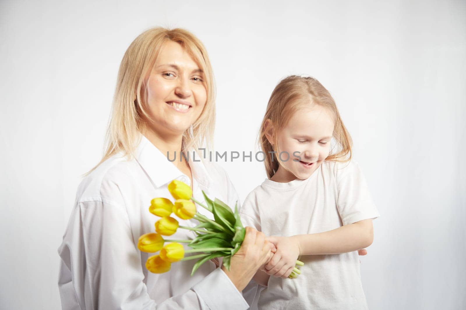 Blonde mother and daughter with a bouquet of tulips on a white background. Mom and girl together on holiday mother's day with flowers. Congratulations to women on International Women's Day on March 8