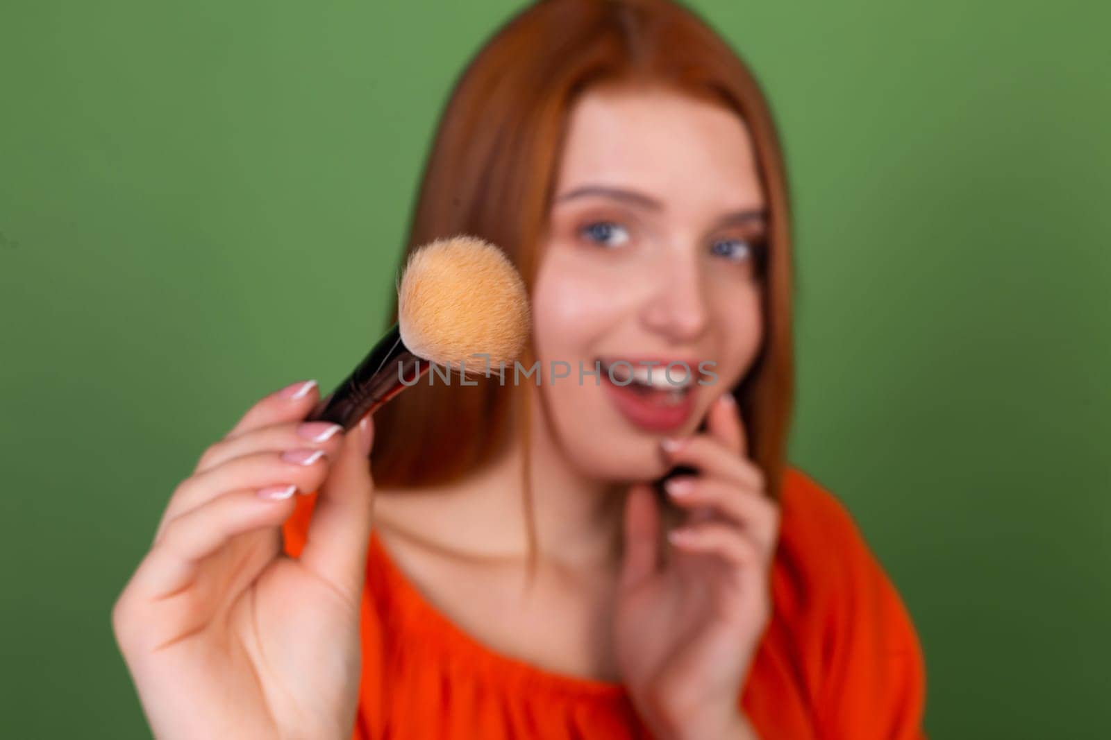 Young red hair woman in casual orange blouse on green background perfect natural smooth skin holding blush brush by kroshka_nastya