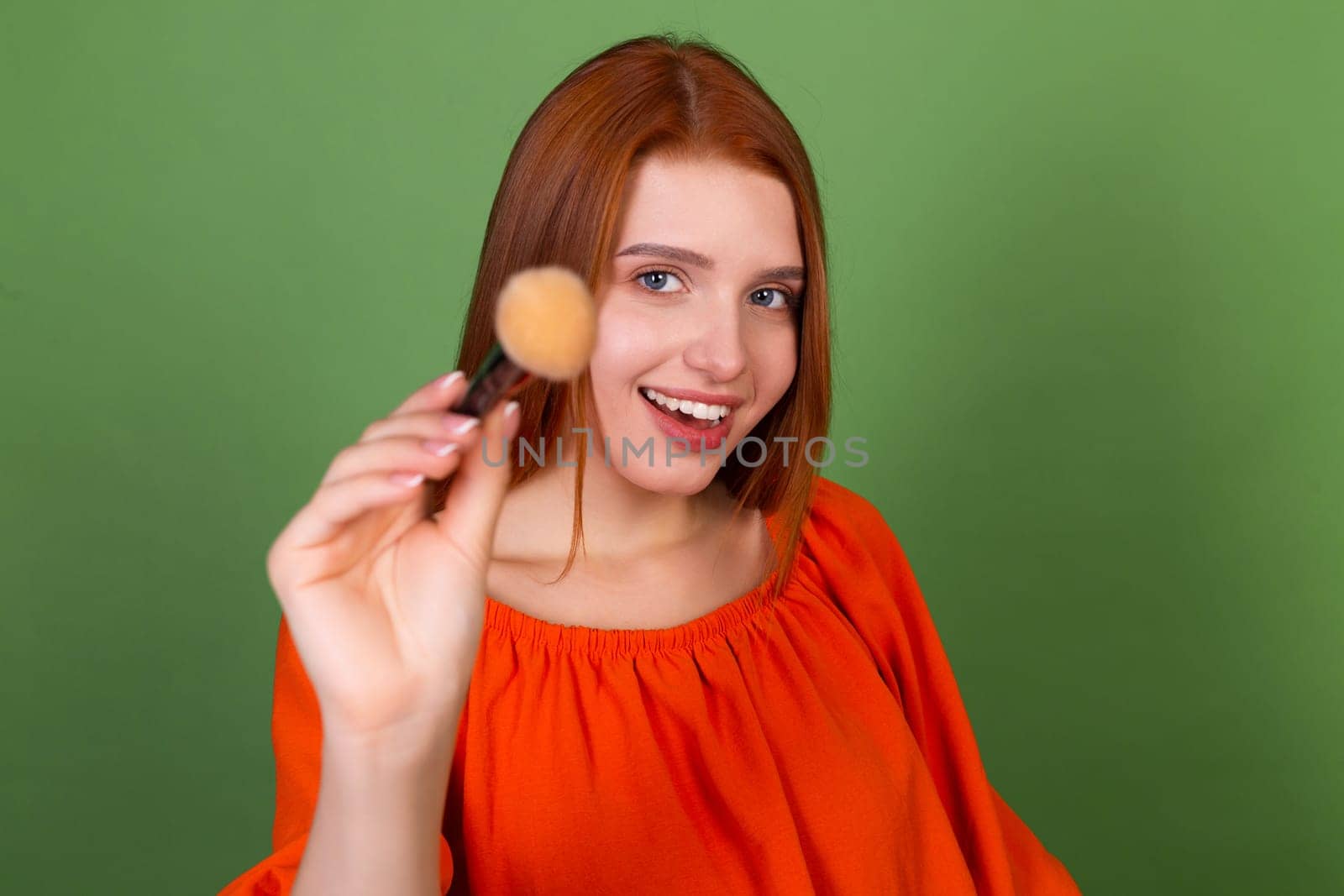 Young red hair woman in casual orange blouse on green background perfect natural smooth skin holding blush brush by kroshka_nastya