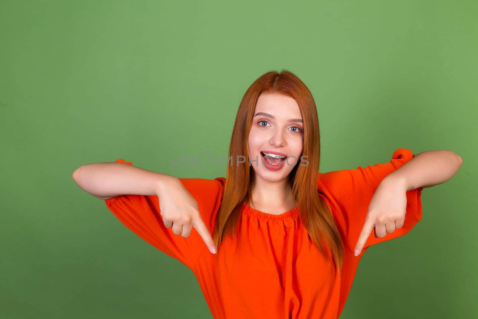 Young red hair woman in casual orange blouse on green background smile and laugh point fingers down by kroshka_nastya