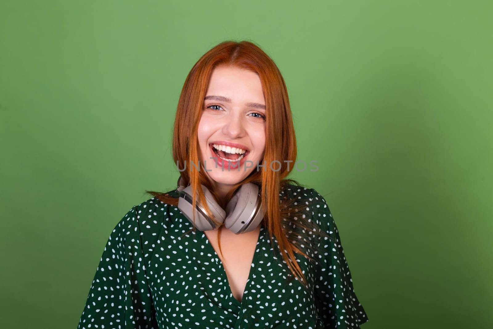 Young red hair woman on green background with wireless headphones happy laugh by kroshka_nastya