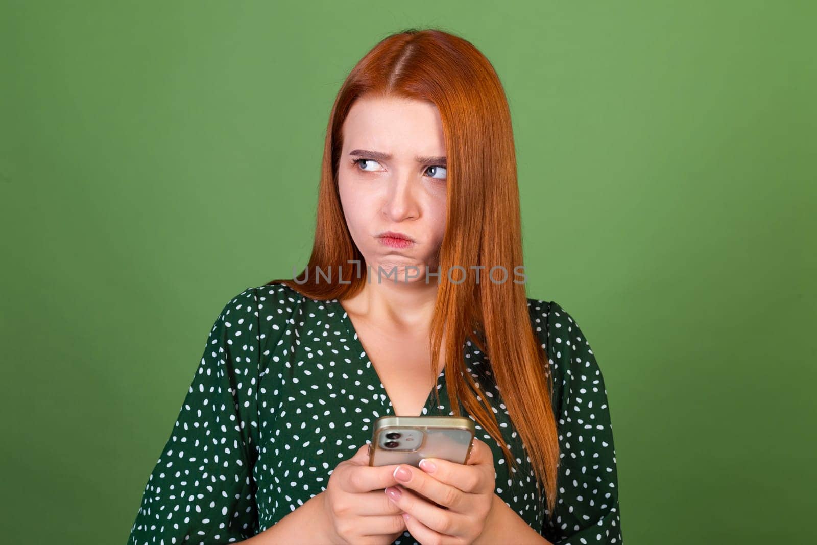Young red hair woman on green background with mobile phone texting chatting angry disappointed serious by kroshka_nastya