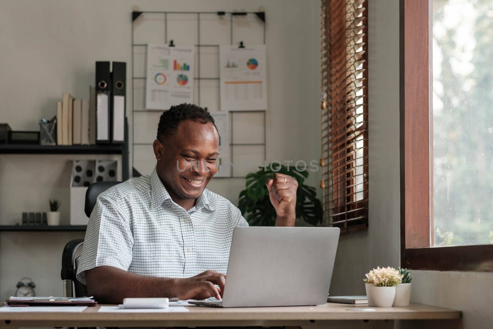 Smiling black man using laptop at home in living room. Happy mature businessman send email and working at home. African american freelancer typing on computer with paperworks and documents on table...