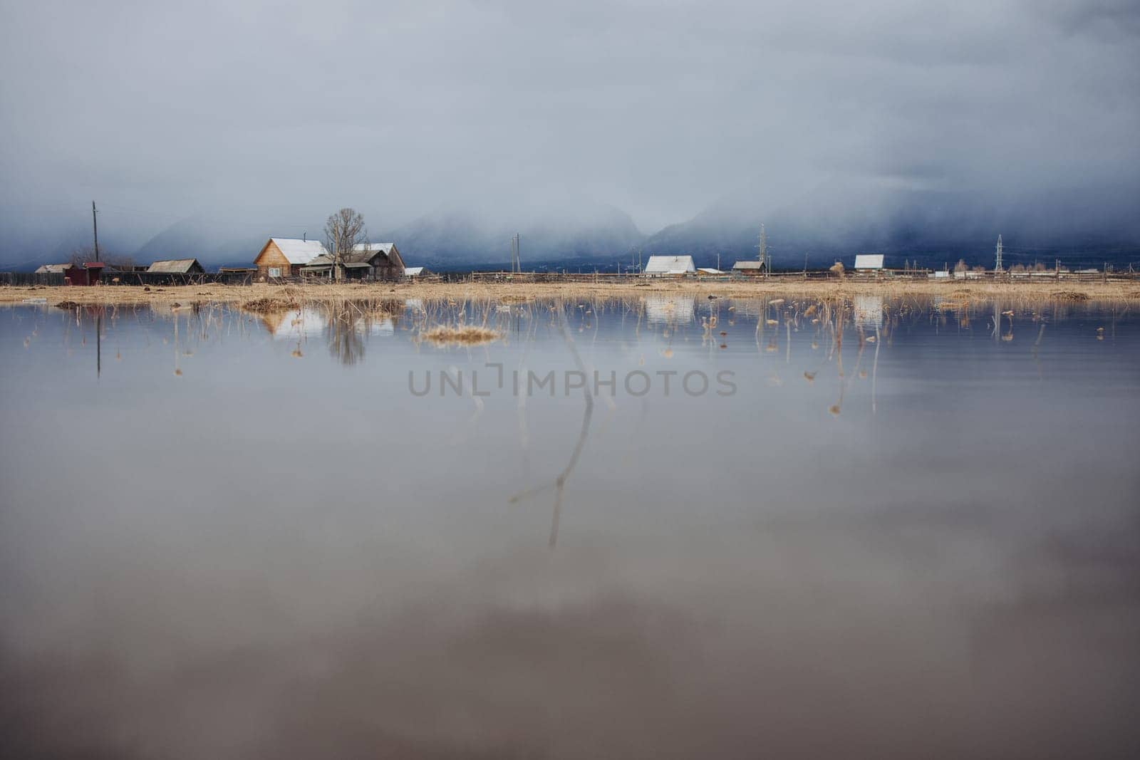 Mirror reflection from the water of melted snow in a Buryat village in dense fog against the backdrop of the Sayan Mountains