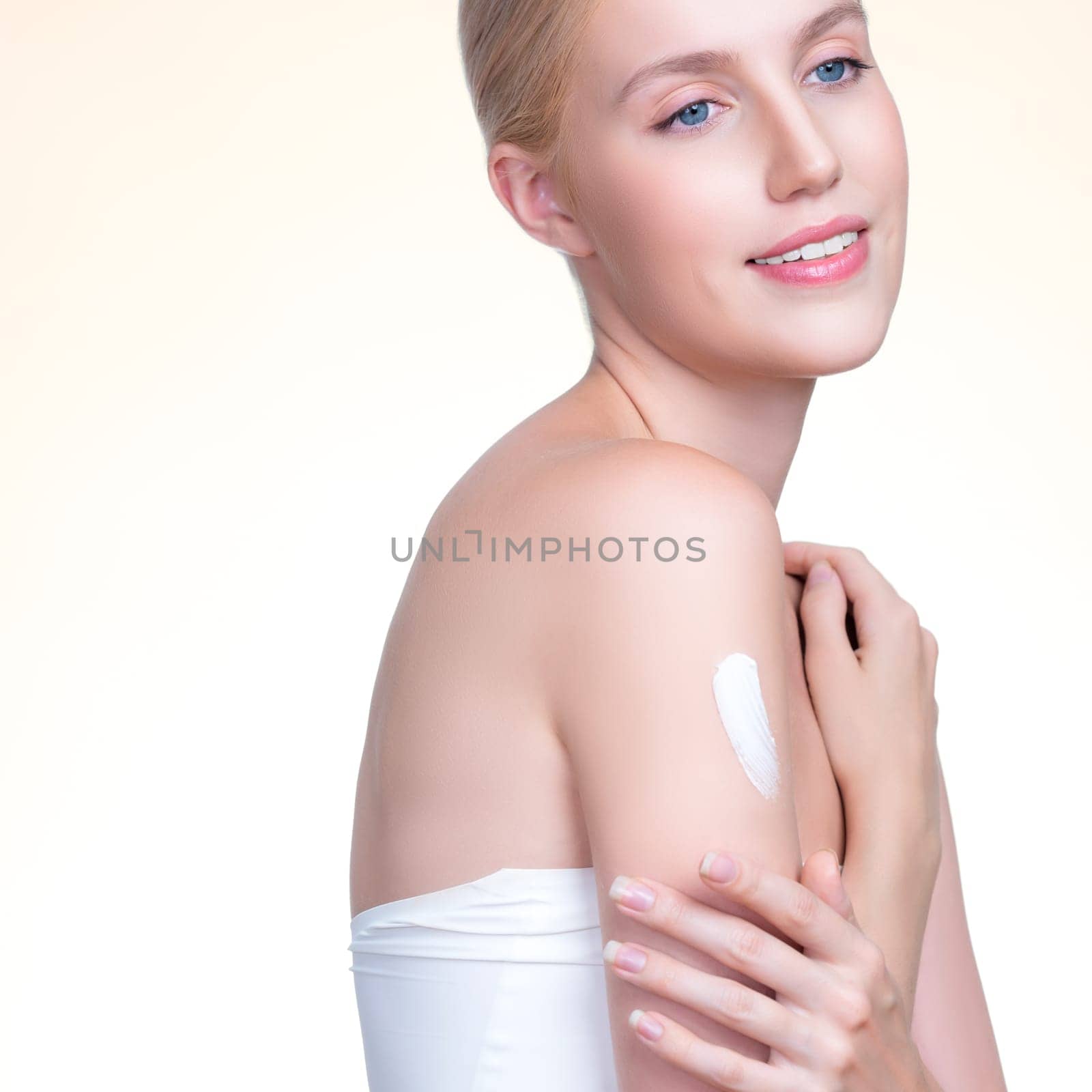 Closeup personable beautiful woman putting skincare moisturizer cream on her arm looking in camera in isolated background as concept for beauty care treatment. Female model applying lotion on her body