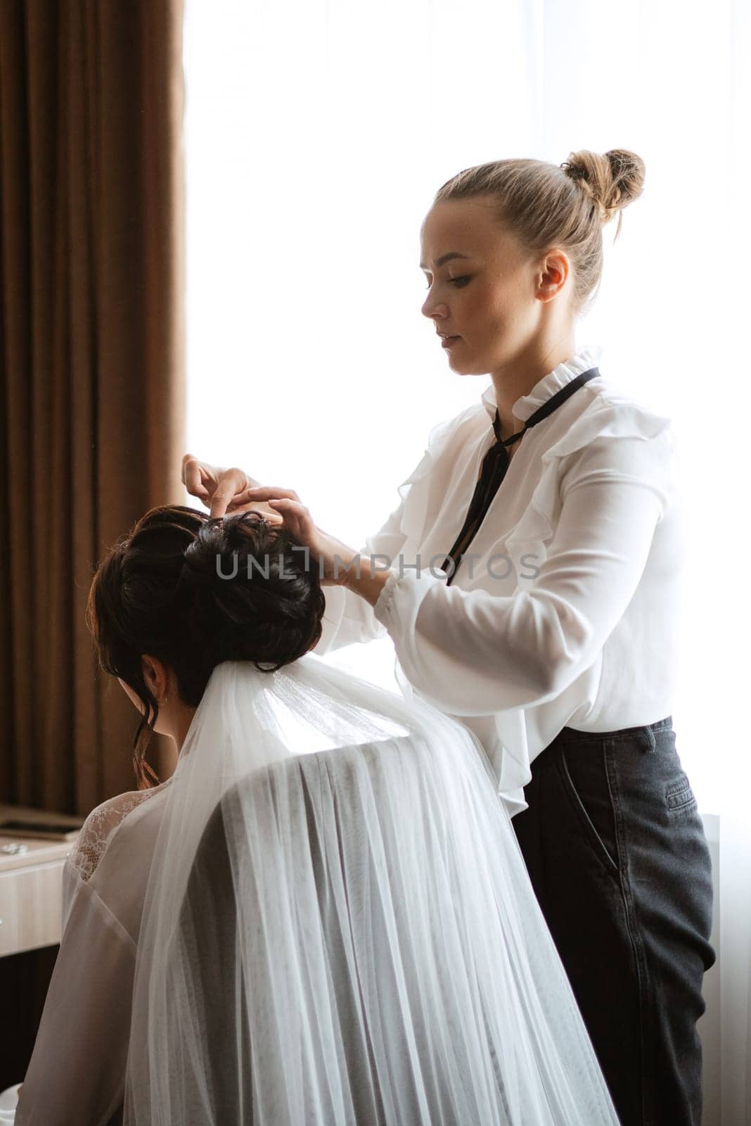 make-up artist makes a wedding look to the bride with makeup and a wedding hairstyle with a veil
